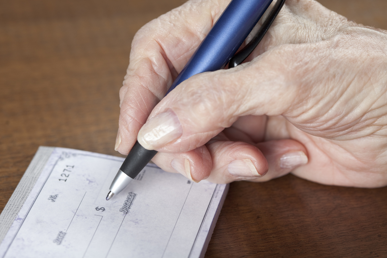 A person’s hand holding a blue pen and writing on a blank check.