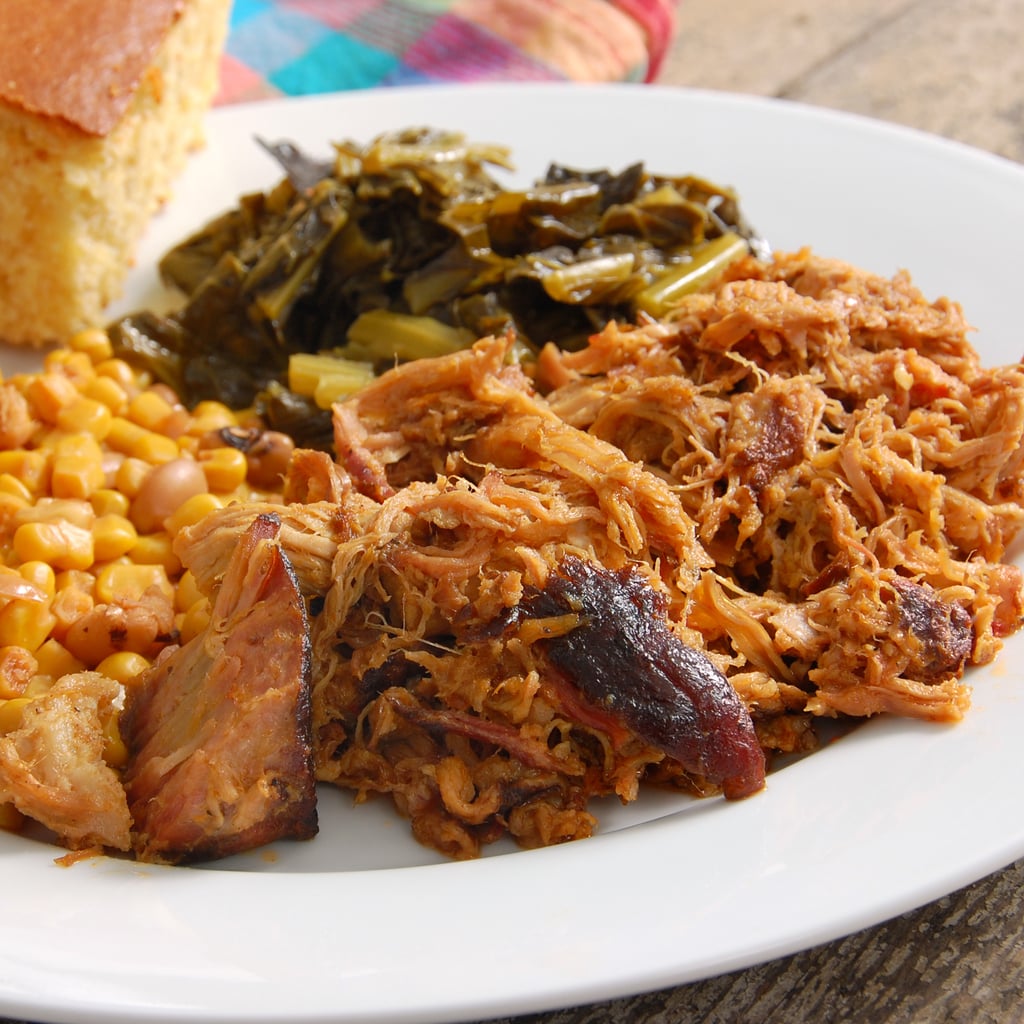 A plate of barbecue pulled pork served with sides of corn and collard greens, with a piece of cornbread on the side.
