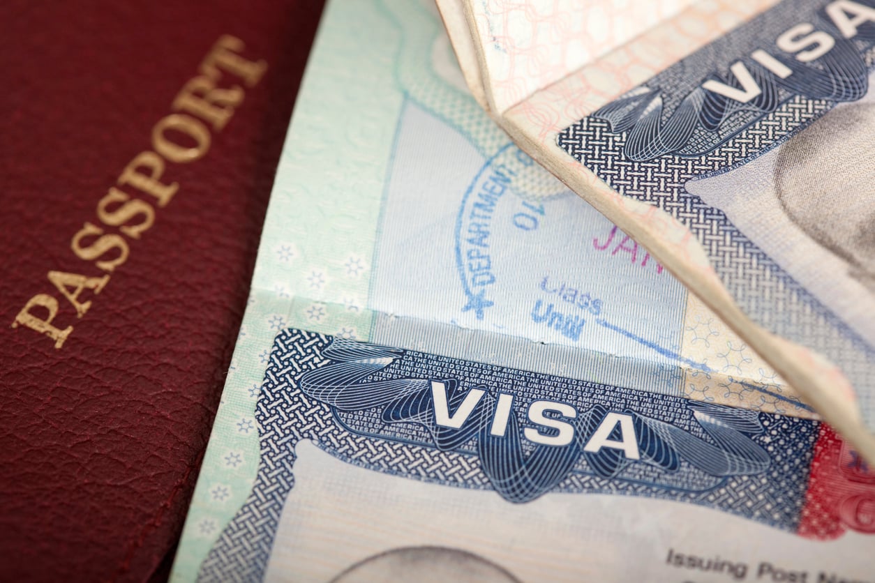 A passport rests next to an open passport page displaying a United States visa, a key element in trip planning decisions.