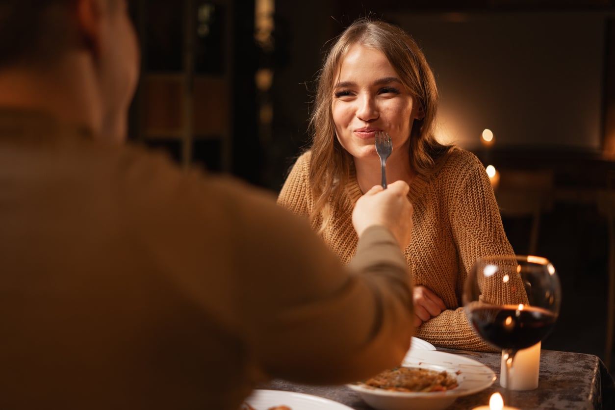 A man feeds a woman a bite of food with a fork during a candlelit dinner.