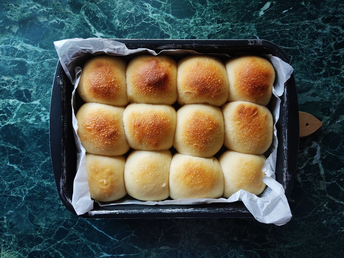 A rectangular baking pan filled with twelve golden-brown dinner rolls lined with parchment paper.