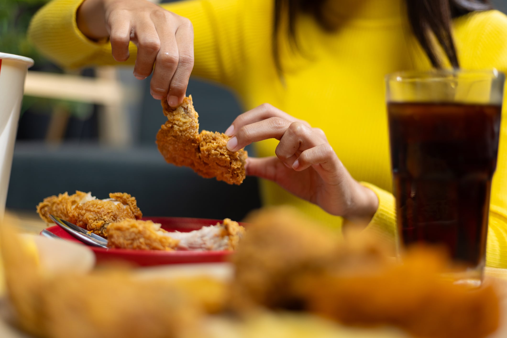 A person wearing a yellow sweater picks up a piece of fried chicken from a plate of breakfast foods.