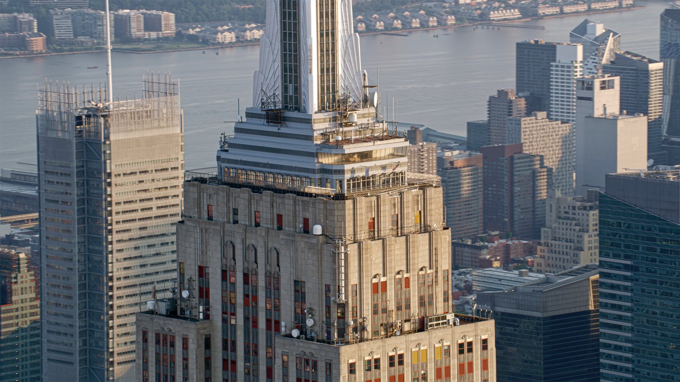Aerial view of the Empire State Building, one of New York’s iconic tourist attractions, surrounded by skyscrapers and a river.