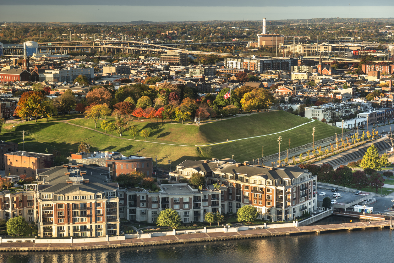 An aerial view of Federal Hill Park in Baltimore, with a grassy hill, autumn foliage, and a surrounding cityscape by the water.