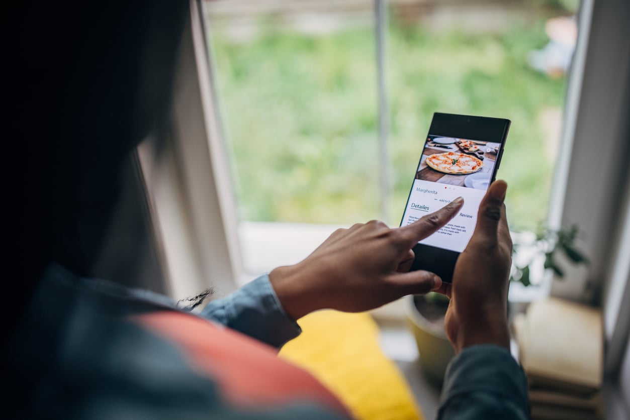 A person uses their finger to scroll through a food delivery app on a smartphone, viewing a product page for a Margherita pizza.