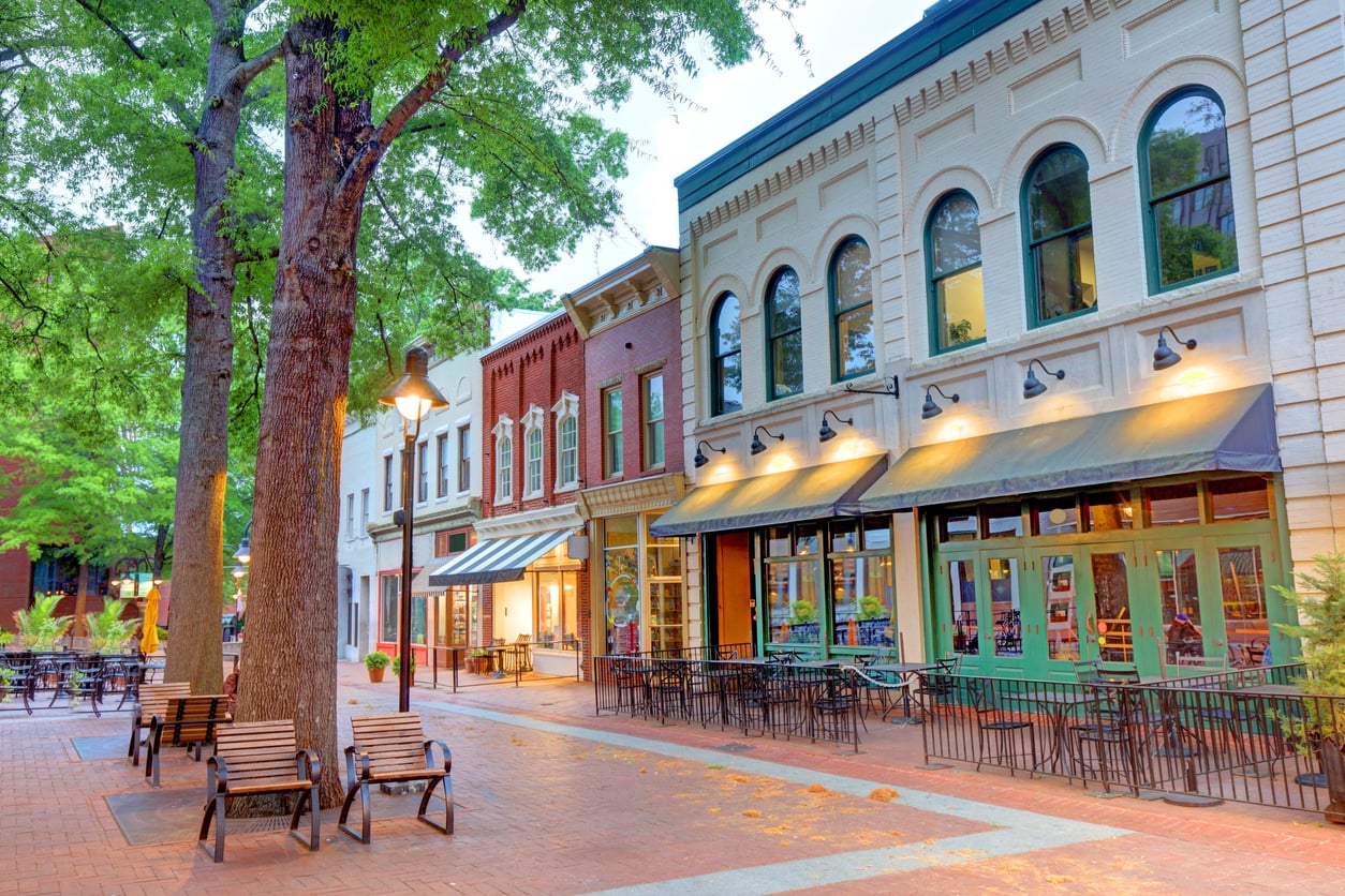 A brick-paved downtown street lined with historic multi-story buildings, outdoor restaurant seating, and large trees.