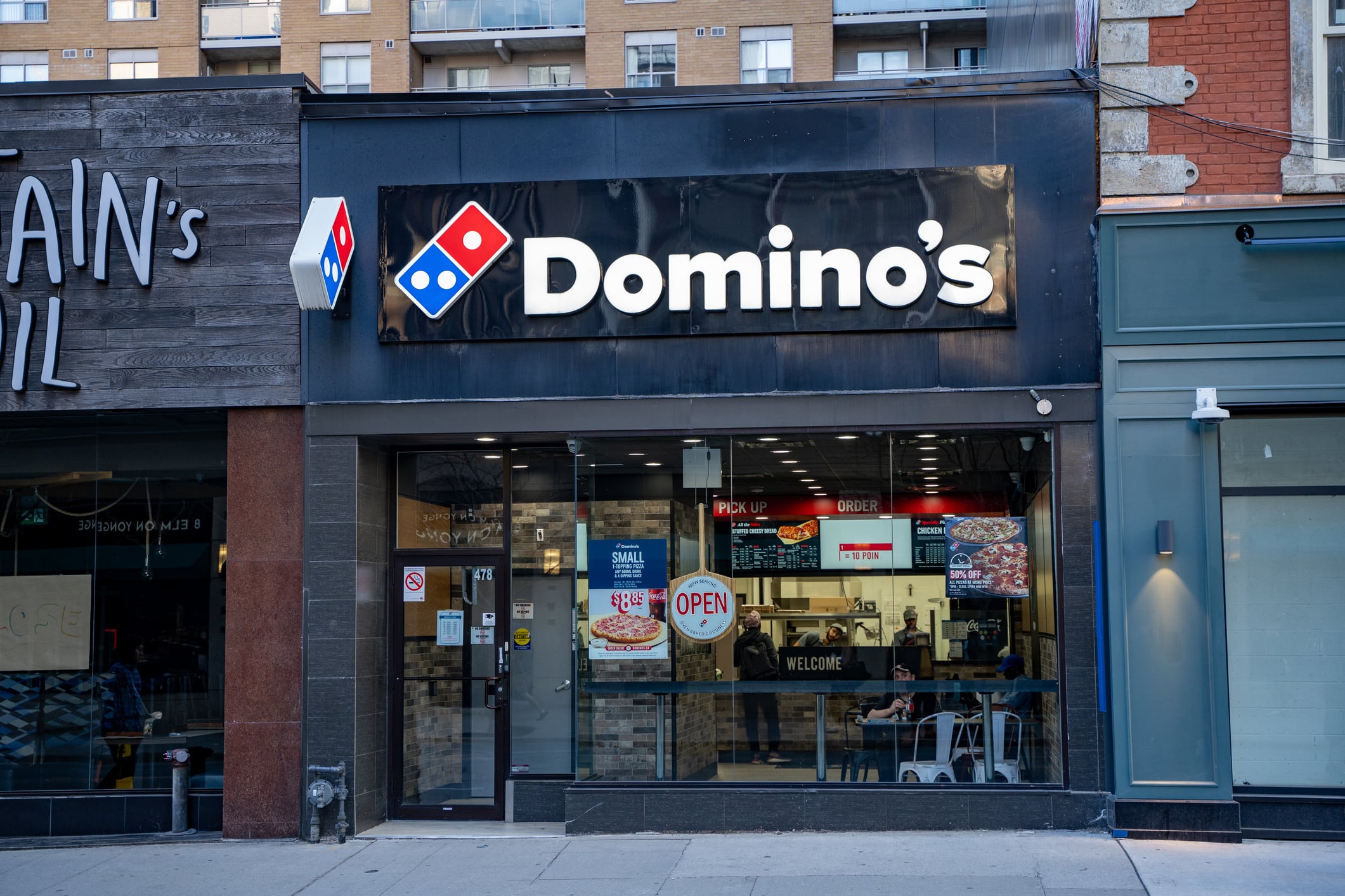 Domino’s storefront with a large logo sign and a window displaying menu specials and an open sign.