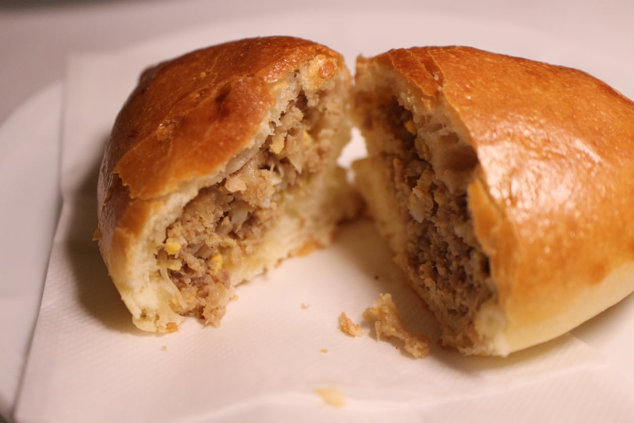 A savory hand pie or pirozhki, cut in half to show a meat and egg filling.