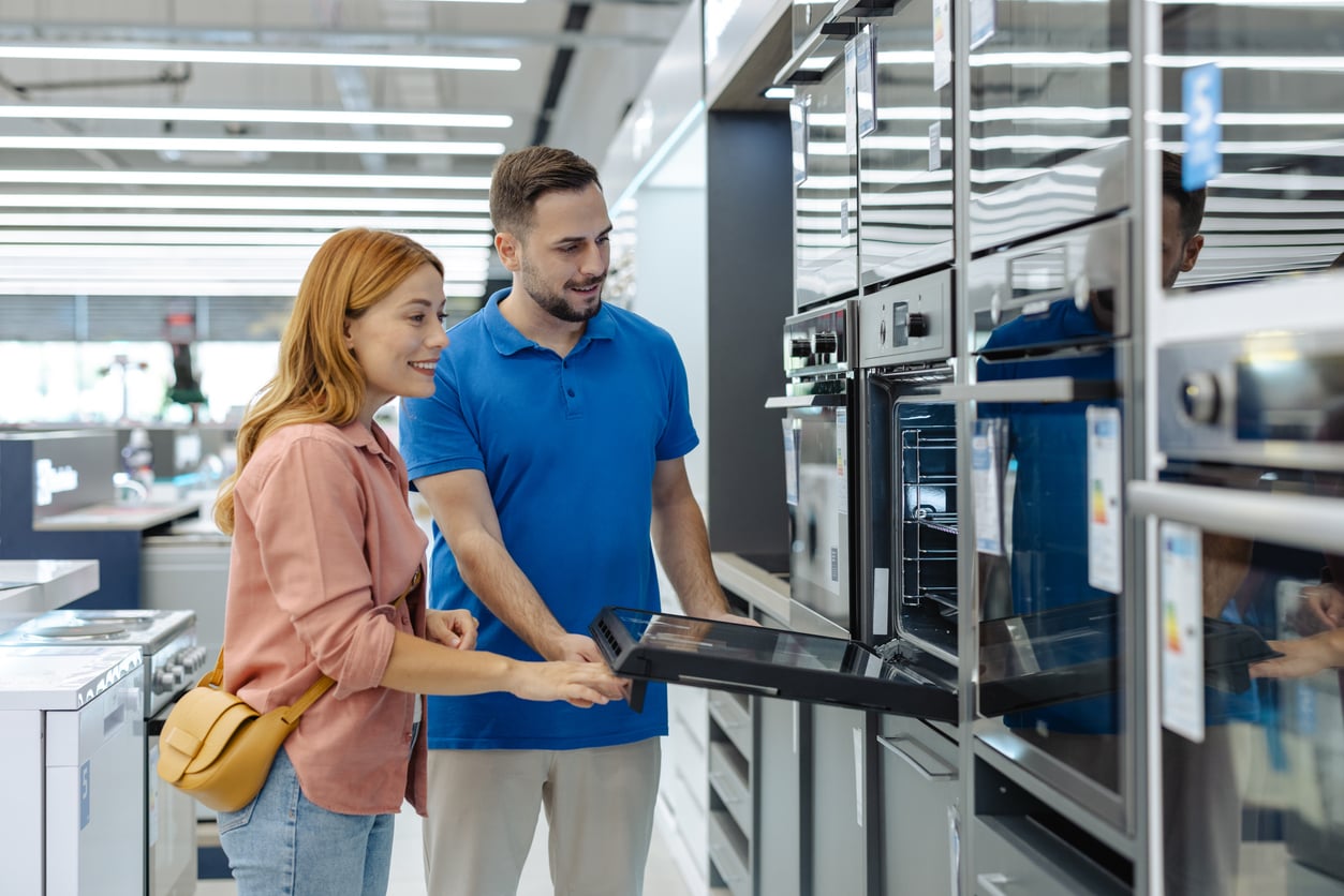 A store employee shows a customer an open wall oven in an appliance showroom.