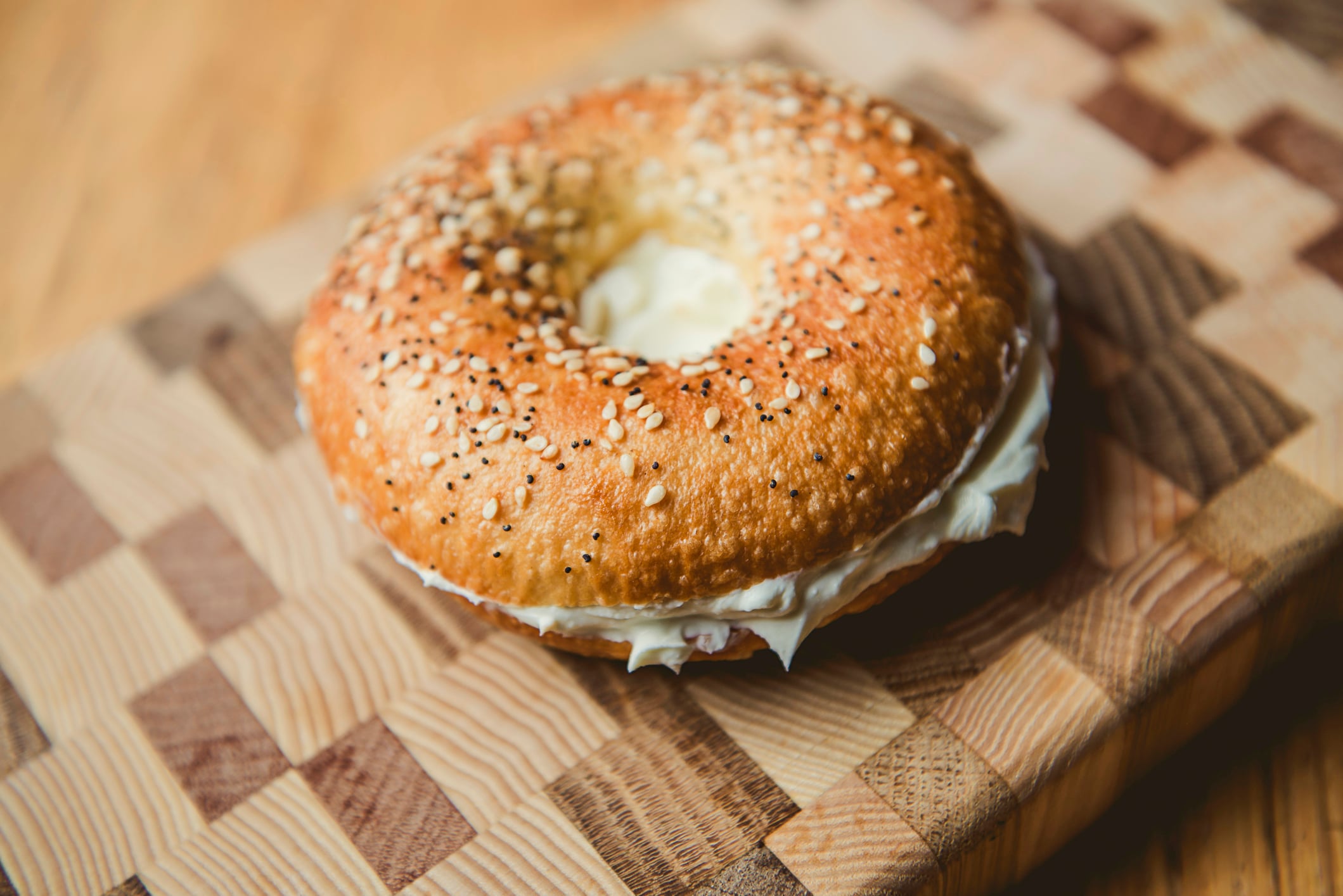 An everything bagel spread with cream cheese on a wooden butcher block cutting board.