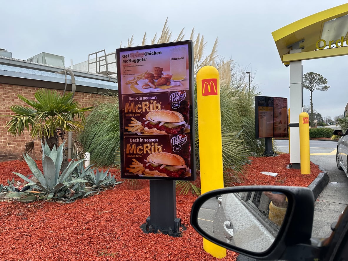 A McDonald’s drive-thru menu board displaying advertisements for Spicy Chicken McNuggets and the McRib sandwich.