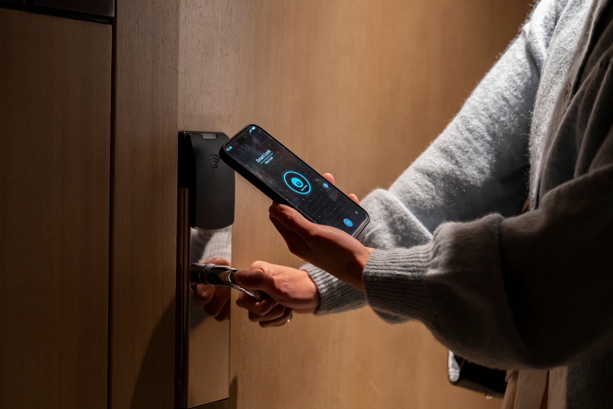 A person holds a smartphone displaying a smart lock app near a digital door lock.