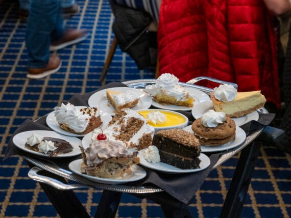 A silver serving tray holding various individual desserts, including slices of pie, cake, a sandwich cookie, and a ramekin of custard, all topped with whipped cream.