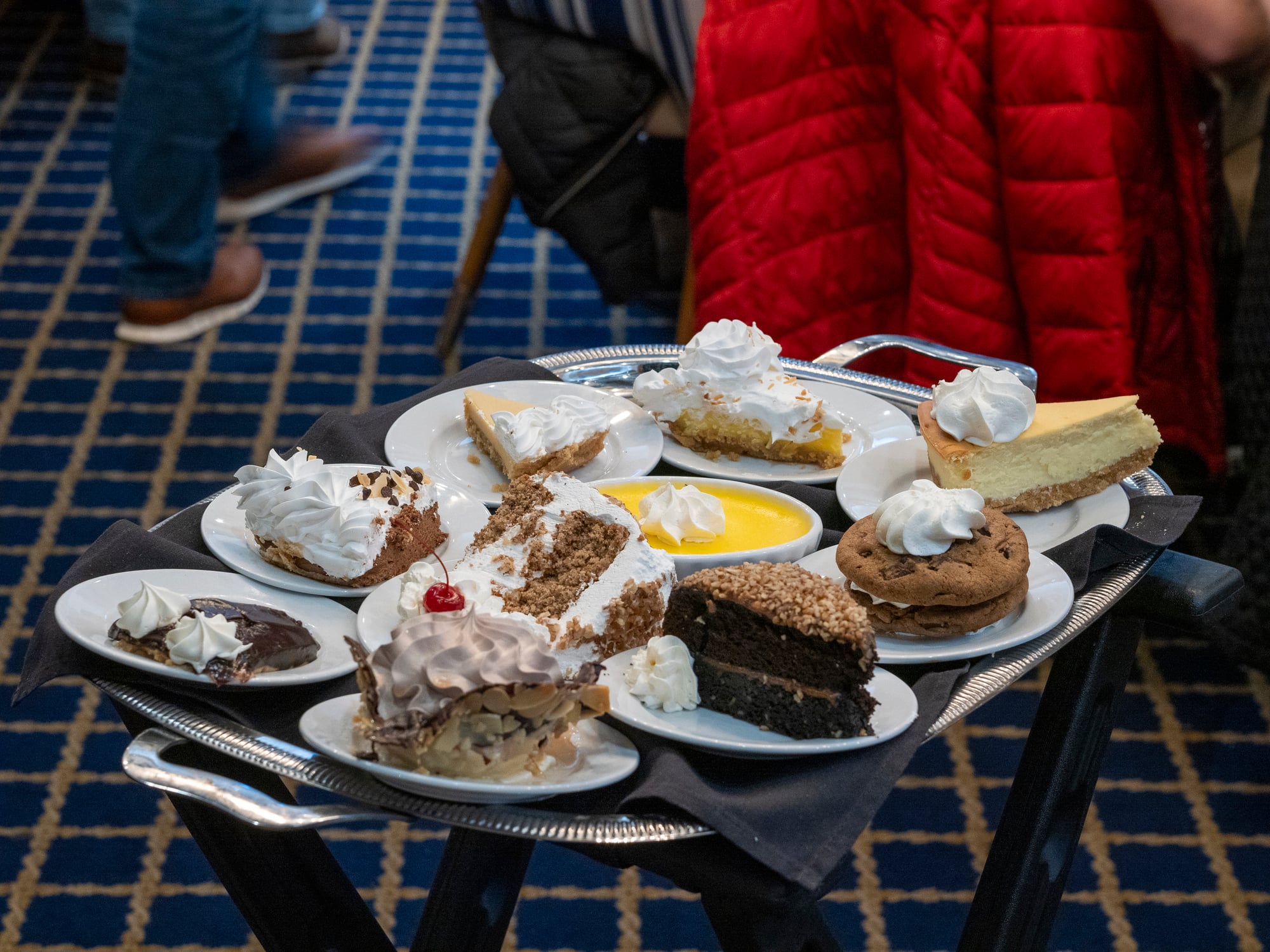 A silver serving tray holding various individual desserts, including slices of pie, cake, a sandwich cookie, and a ramekin of custard, all topped with whipped cream.