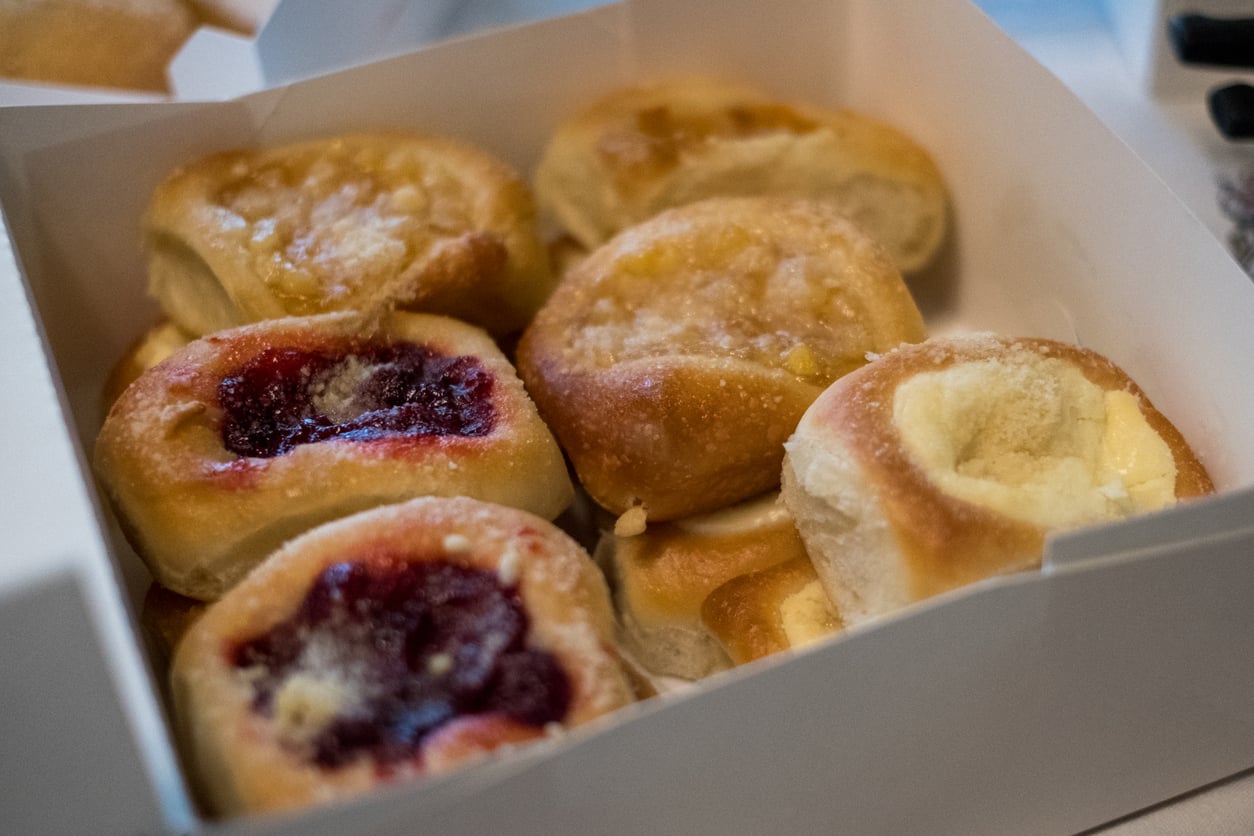 A white box filled with assorted small pastries, including some topped with fruit jam and others with a cream filling.