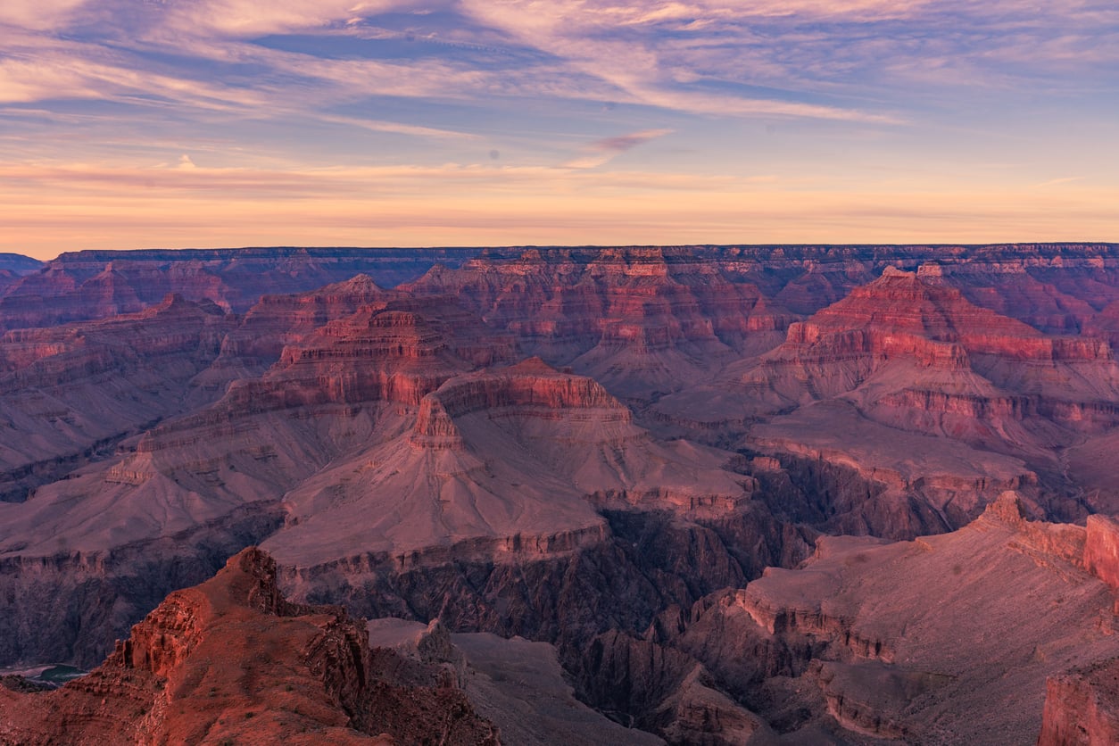 Expansive view of the Grand Canyon under a sunset sky with pink and orange clouds.
