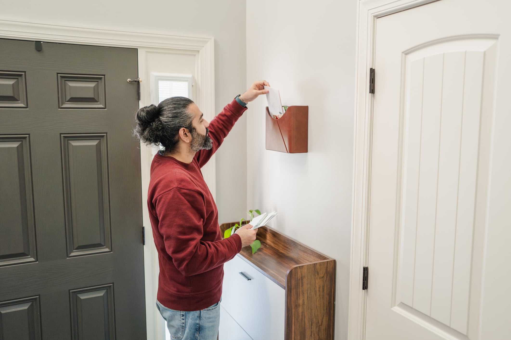 A man placing mail into a wall-mounted leather organizer in an entryway, perfect for home improvements.