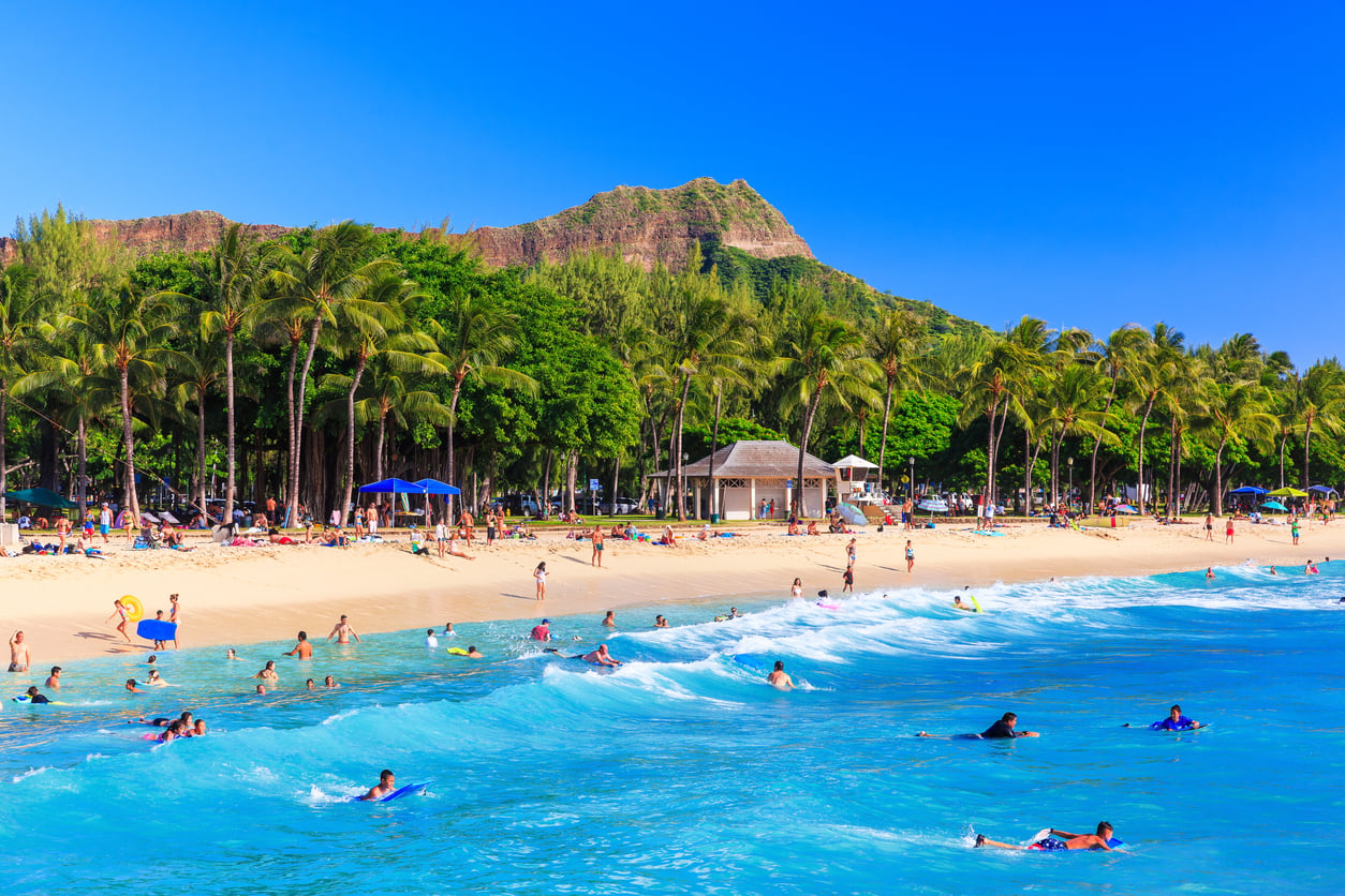 People swimming and surfing at Waikiki Beach with Diamond Head crater in the background.