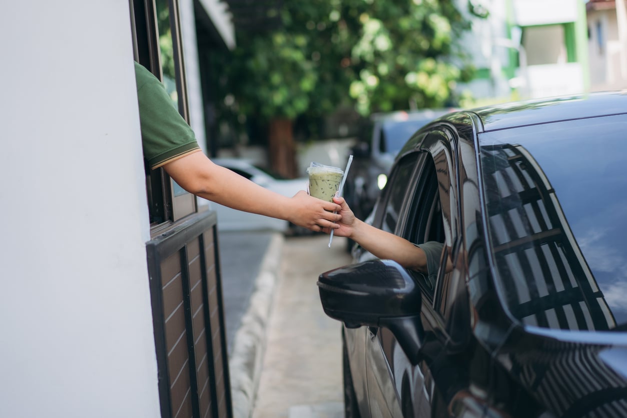 A drive-thru employee hands an iced green tea to a customer in a car.