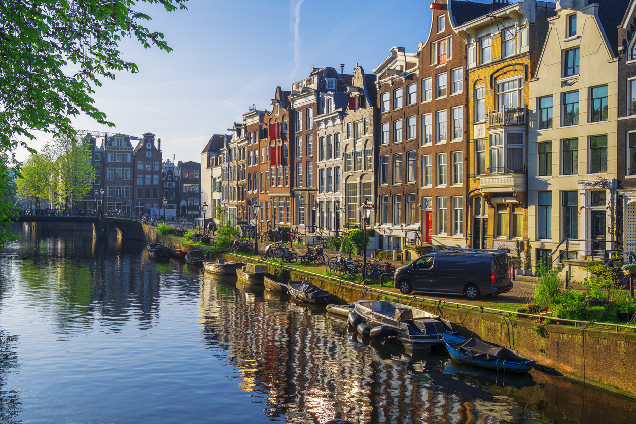 A canal in Amsterdam lined with narrow historic buildings, docked boats, and bicycles parked along the water’s edge, evoking trips that feel luxurious.