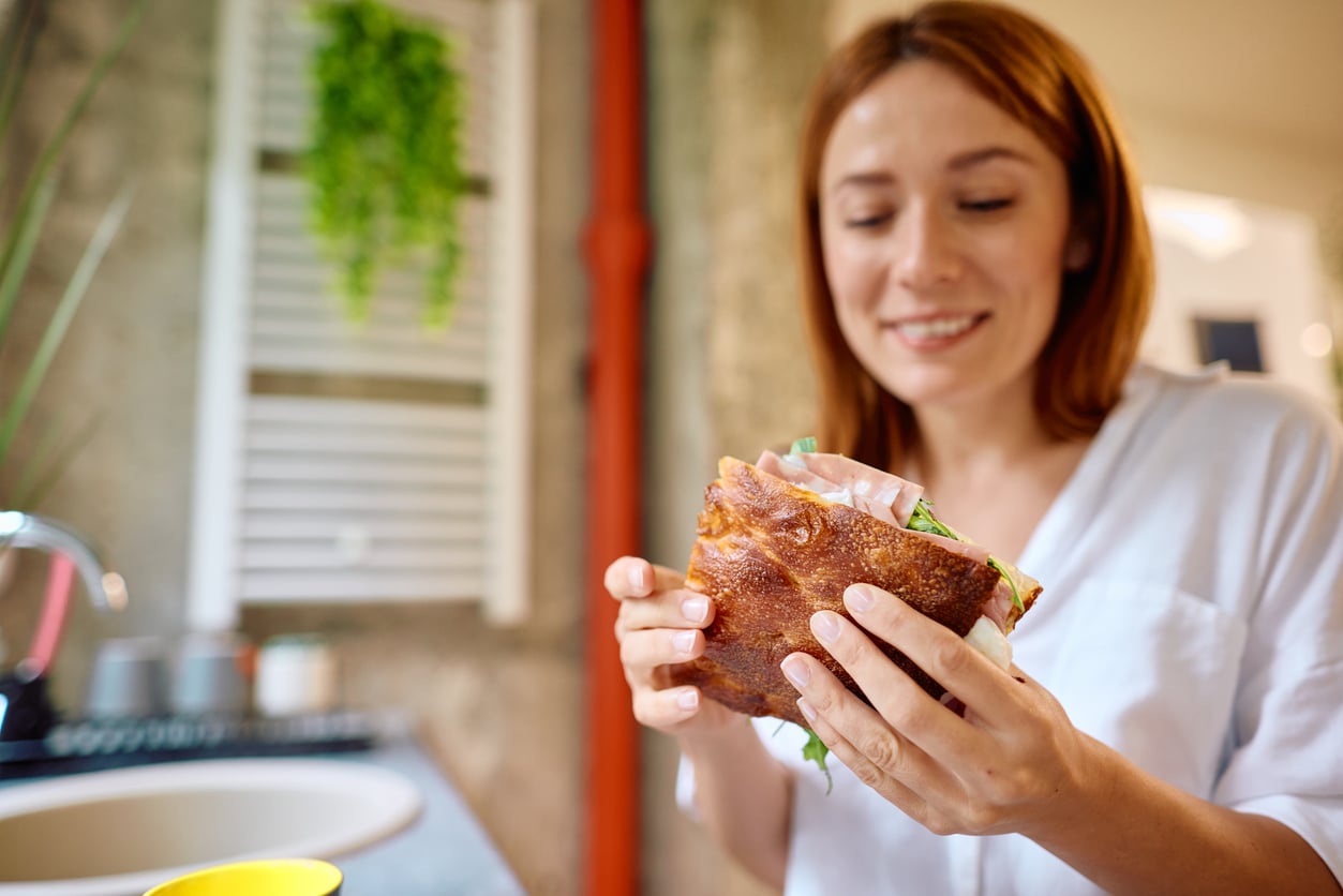 A woman smiles while holding a focaccia sandwich with ham and greens.