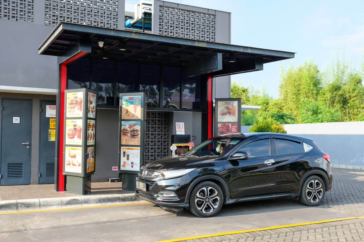 A black car parked at a restaurant drive-thru ordering station.