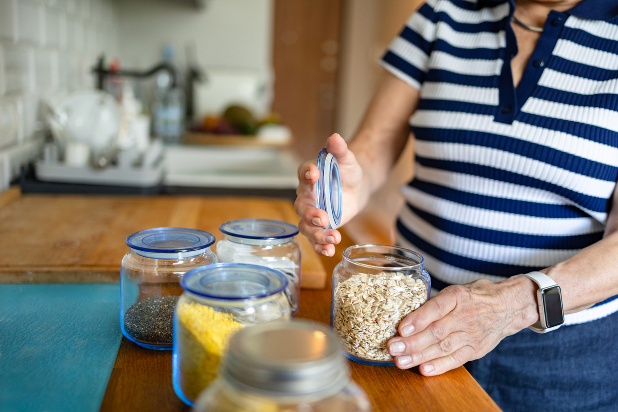 A person wearing a striped shirt opens a glass jar filled with rolled oats on a kitchen counter.