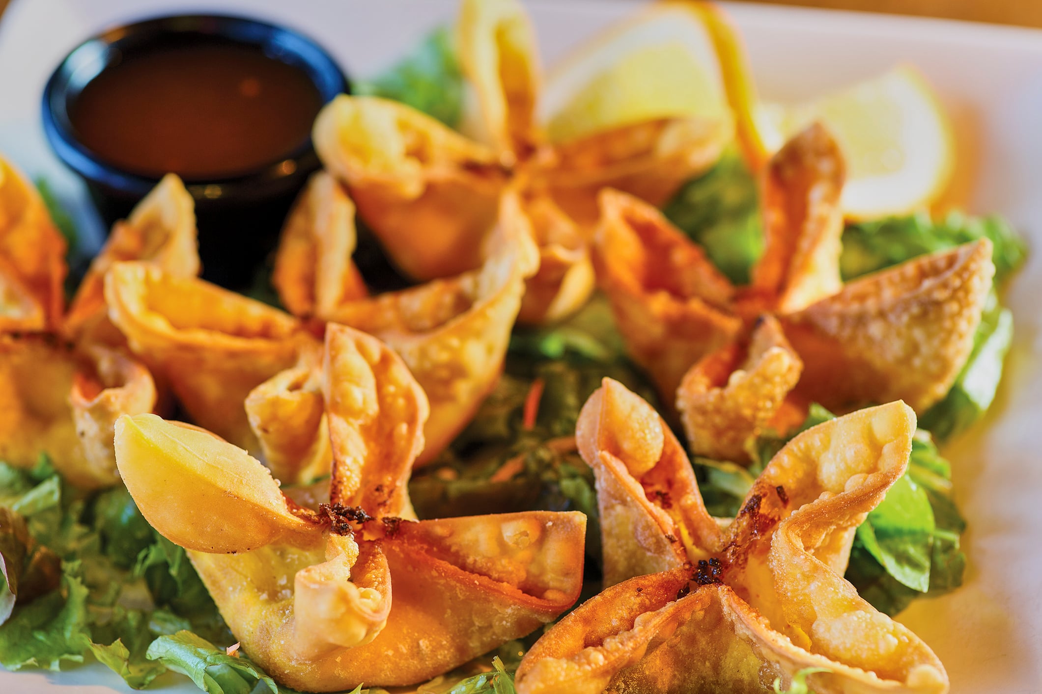 Fried wontons served on a bed of lettuce with a side of dipping sauce and lemon wedges.
