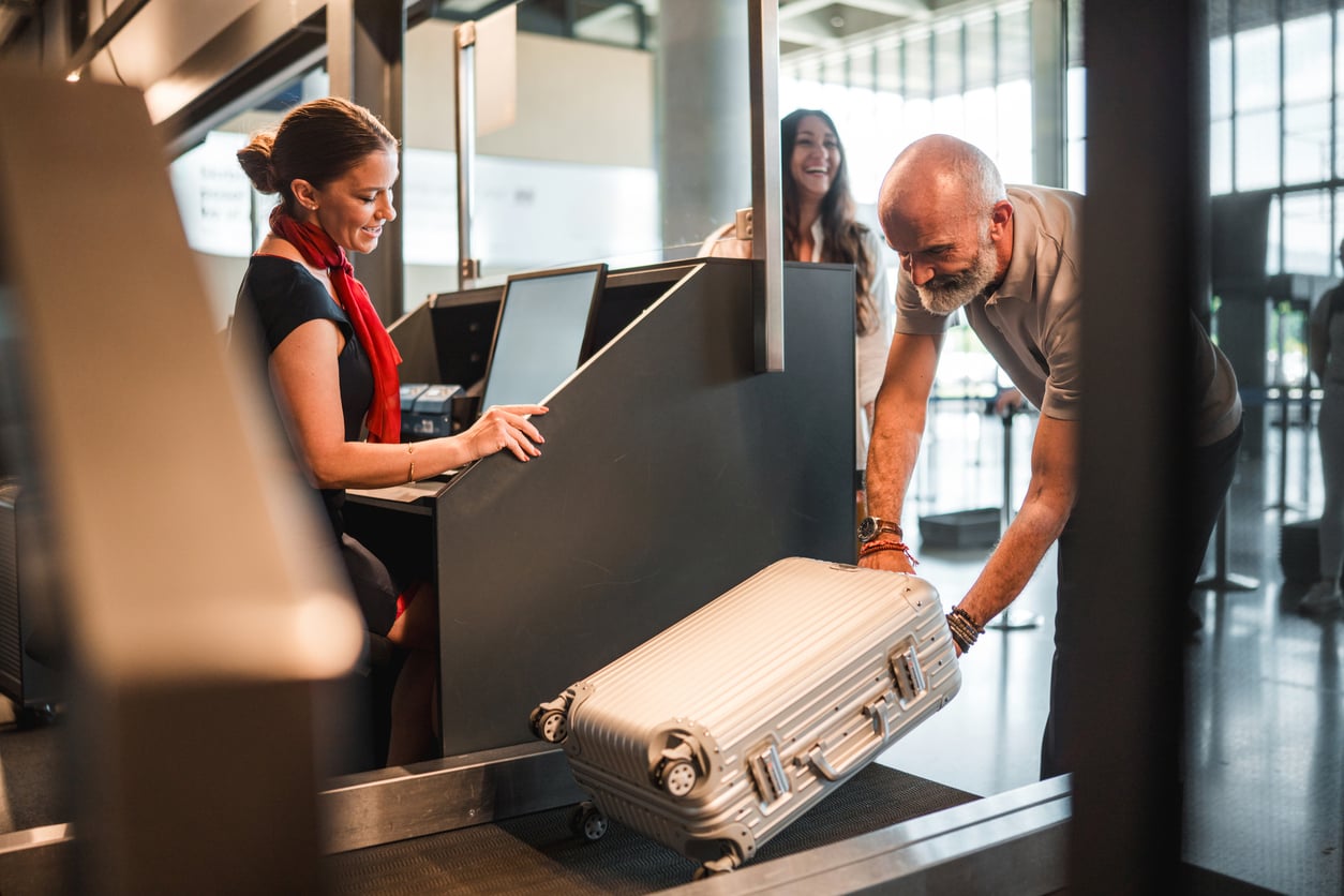 An airline employee assisting a man placing a suitcase onto a luggage scale at a check-in counter.