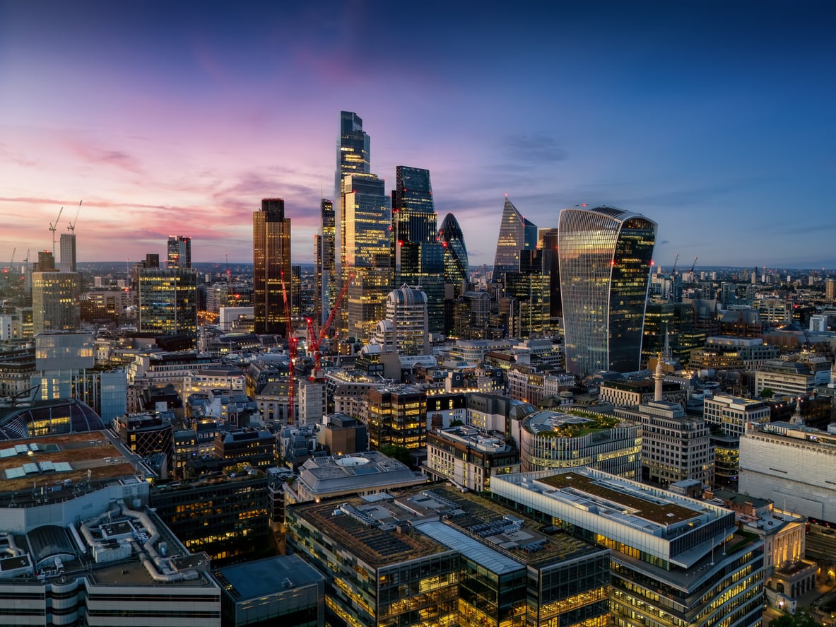 Aerial view of the London city skyline at dusk with illuminated skyscrapers.