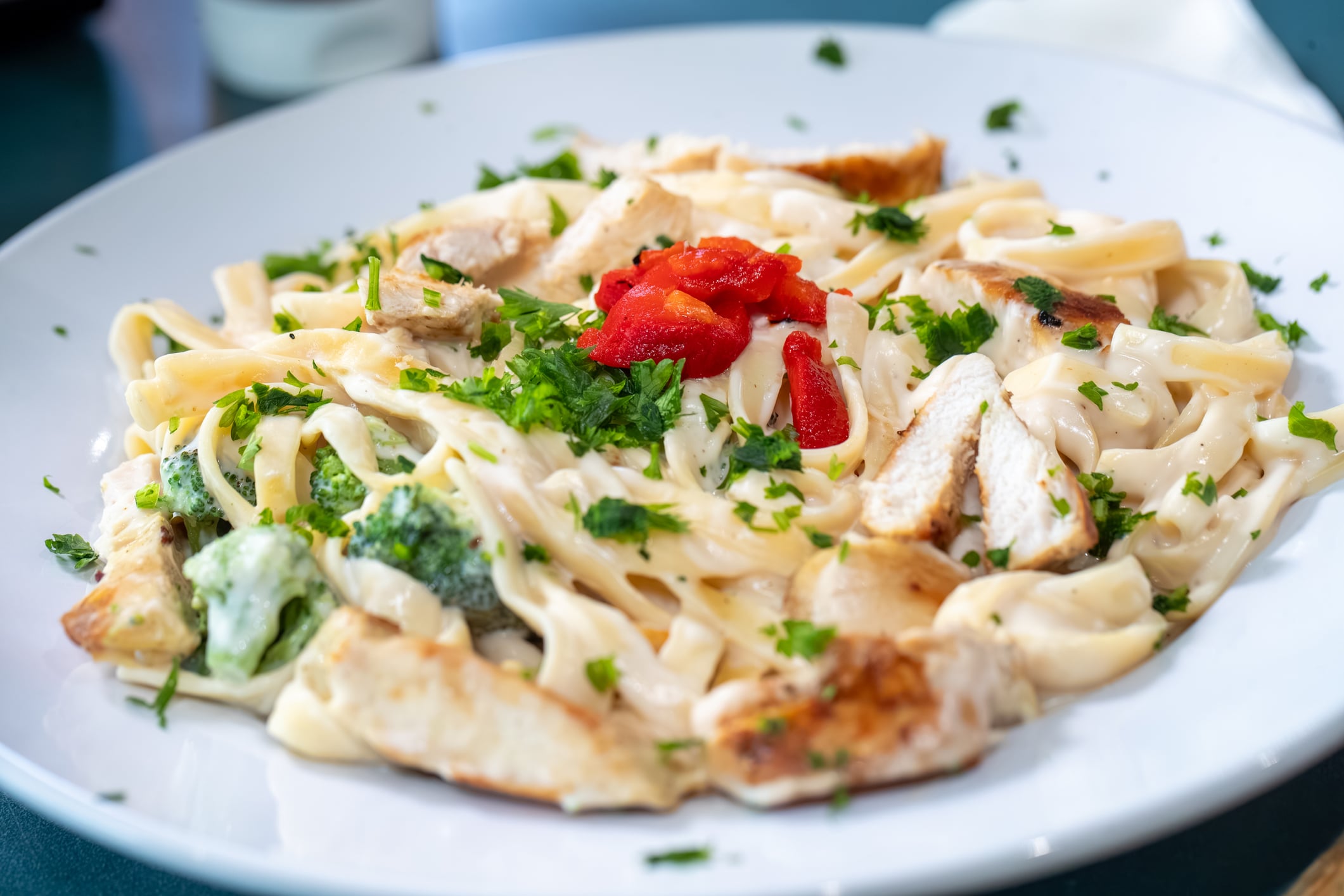 American versions of international foods : A plate of chicken fettuccine alfredo with broccoli, garnished with fresh herbs and roasted red peppers.