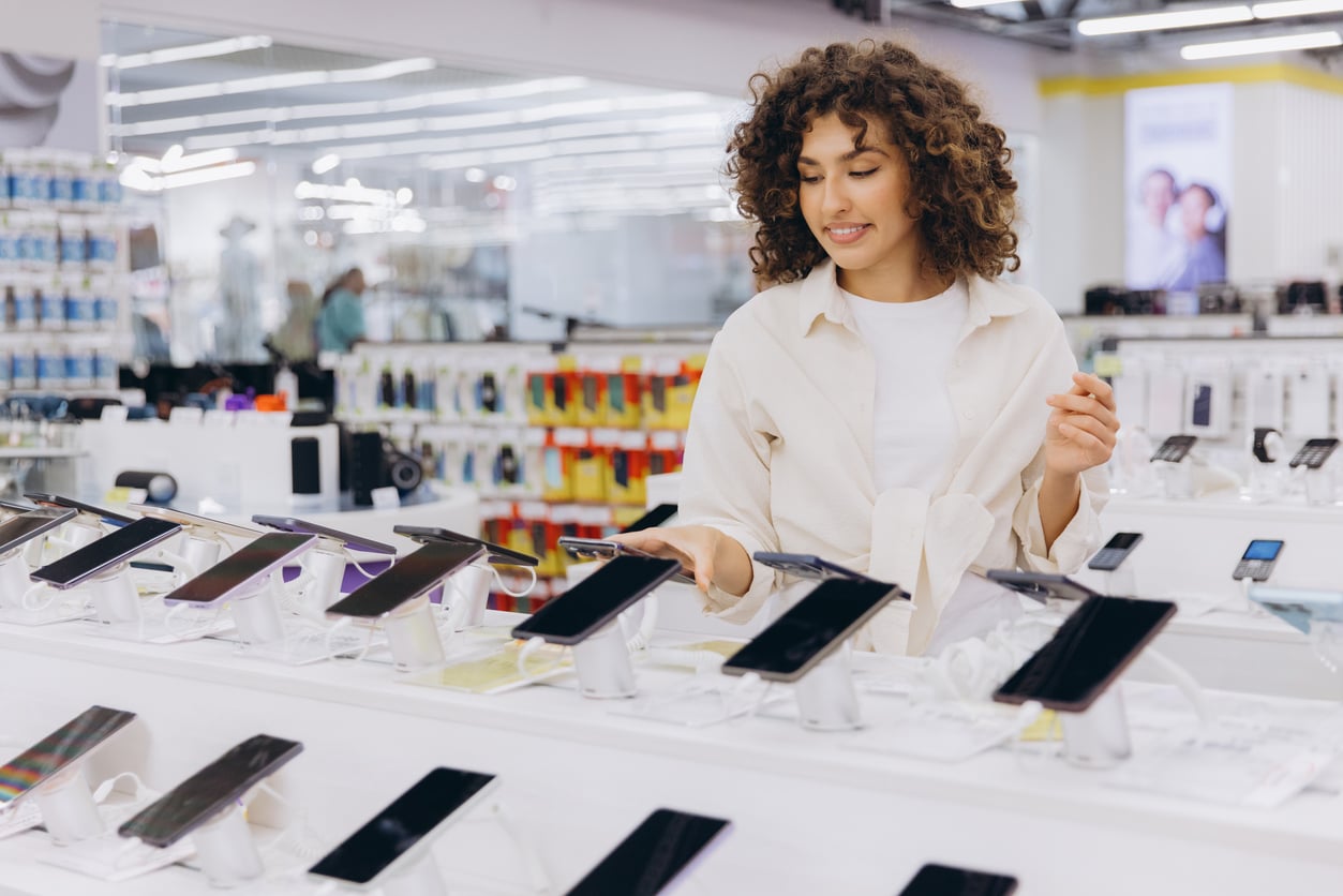 A woman with curly hair looking at and touching a display of smartphones in a store.