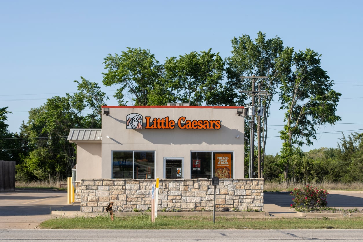 A Little Caesars restaurant with a stone-accented exterior and a sign advertising that the pretzel crust is back.