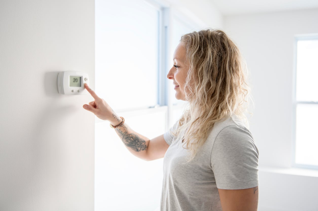 A woman adjusting a wall-mounted digital thermostat.