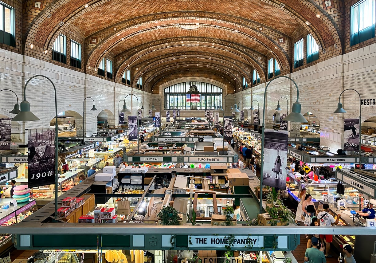 Elevated view of a bustling historic indoor market hall featuring a vaulted tiled ceiling and rows of vendor stalls with hanging banners.