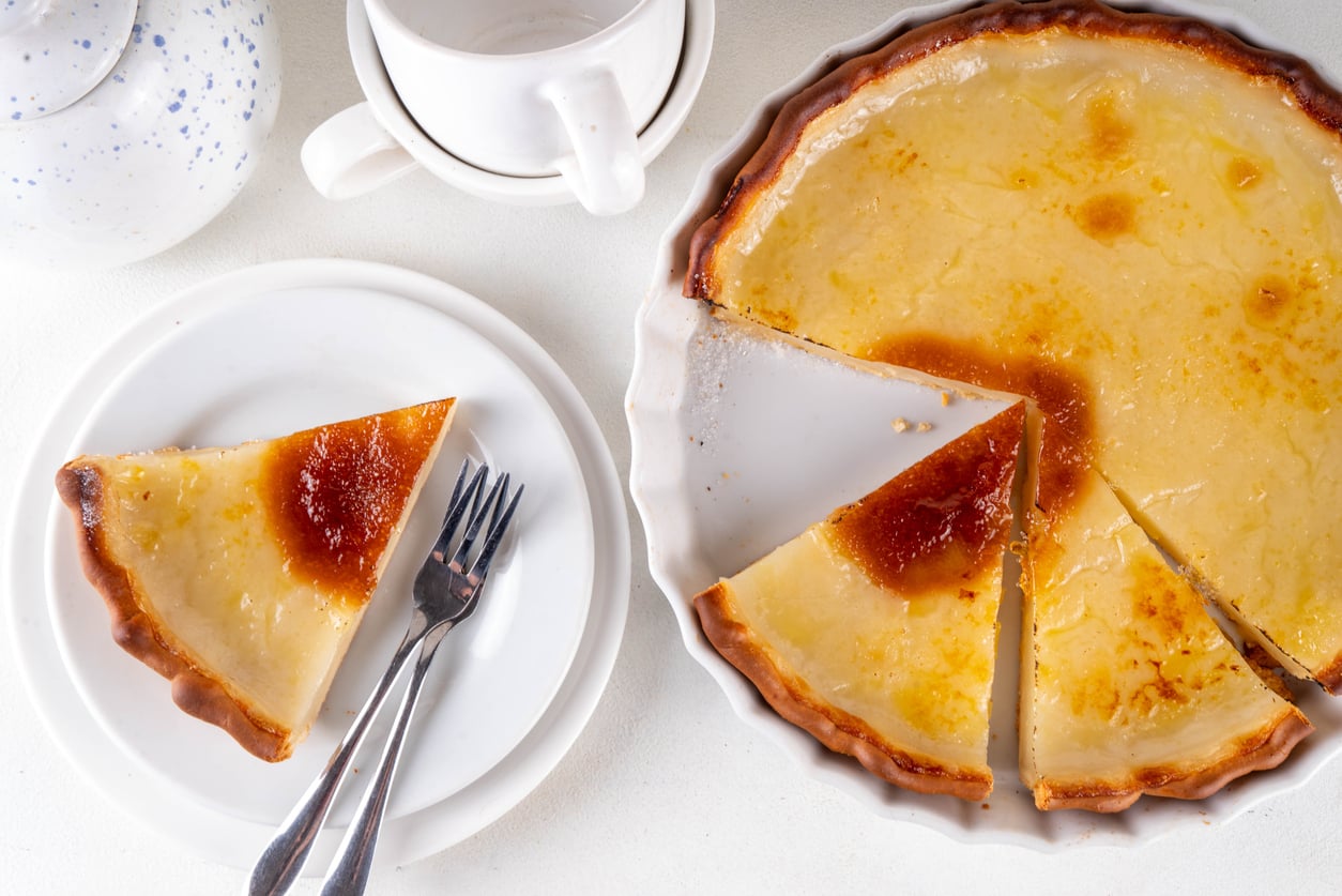 A baked custard tart in a fluted dish with a slice served on a plate next to a fork.
