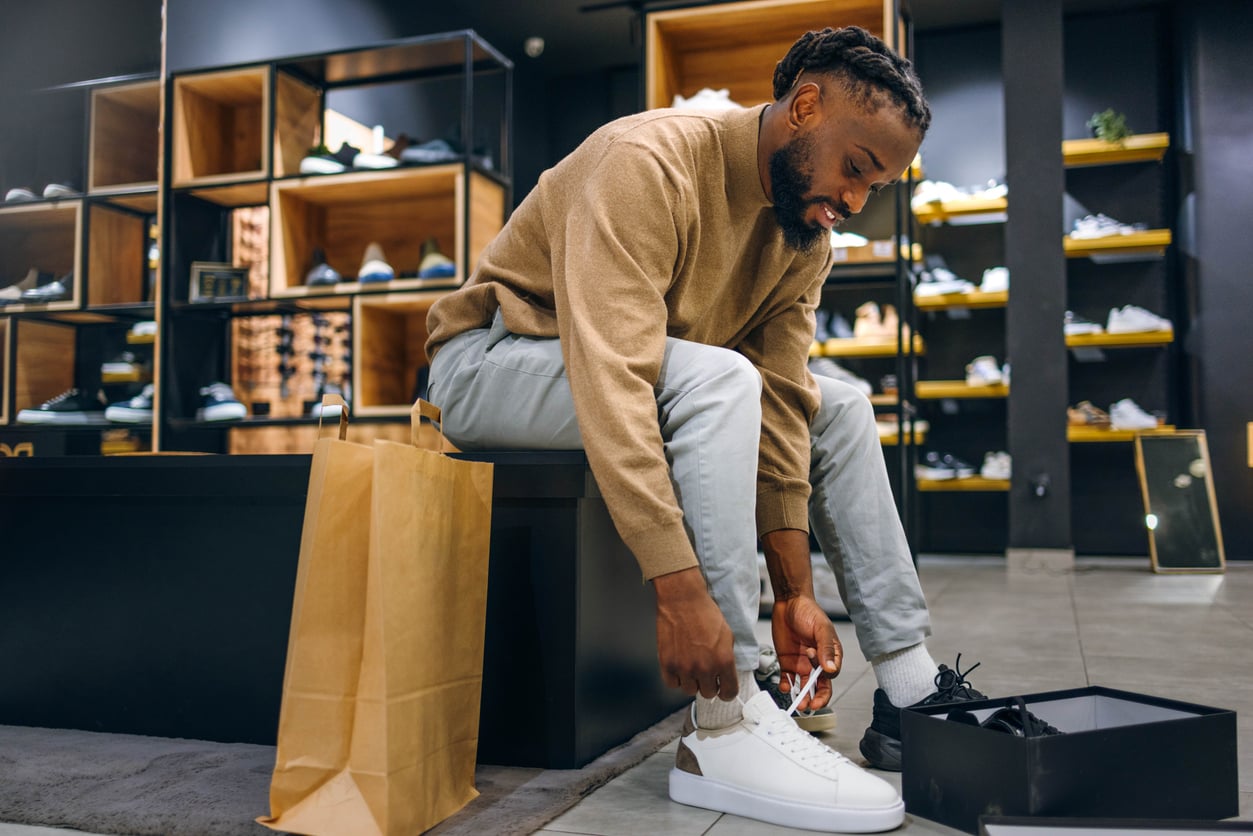 A man sitting in a shoe store trying on a white sneaker.