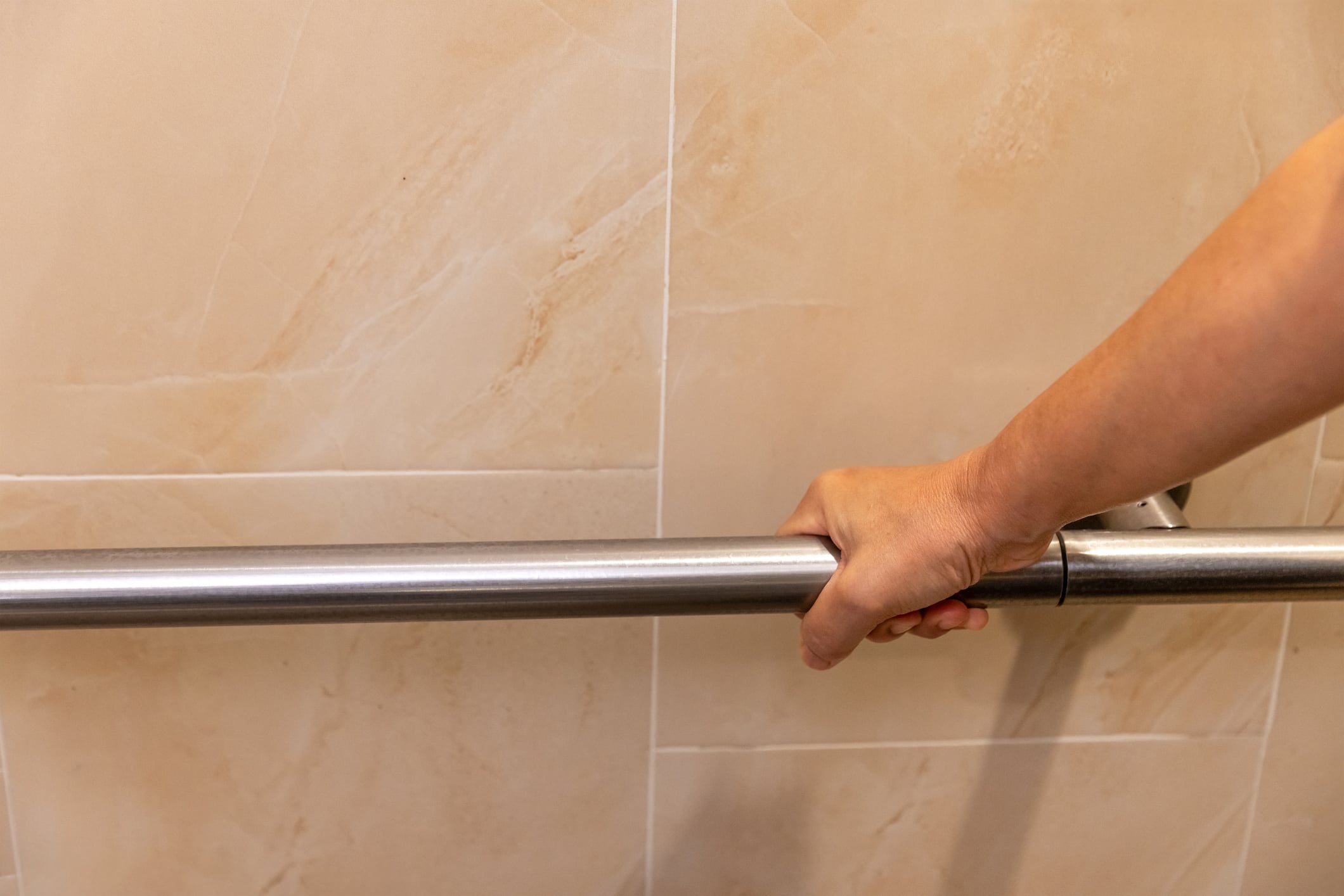 A hand gripping a horizontal metal grab bar mounted on a tiled wall.