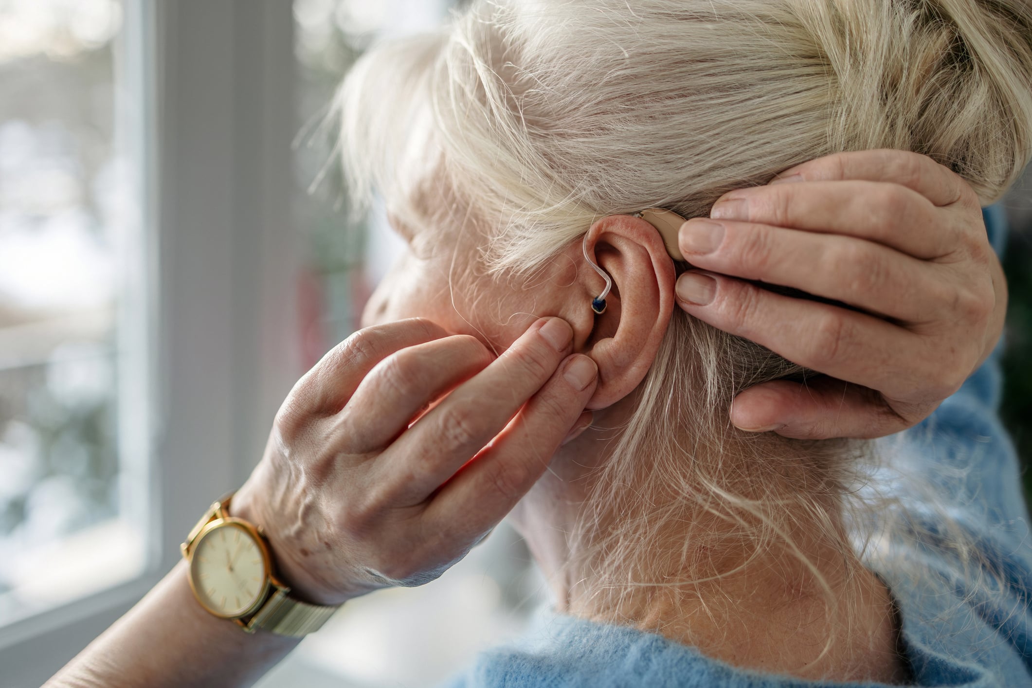 An older woman adjusting a hearing aid in her ear.