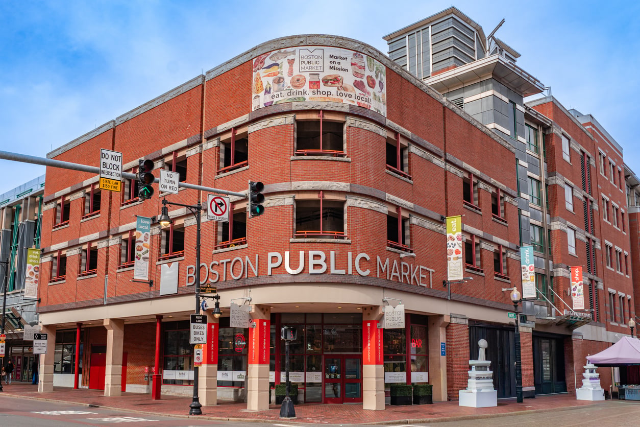 The Boston Public Market building, a red brick multi-level structure on a corner, with signage advertising “eat. drink. shop. love local.”