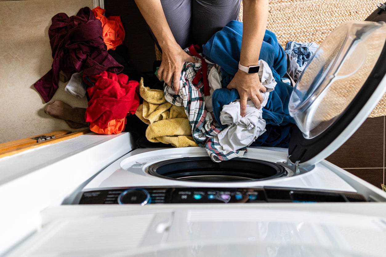 A person putting a pile of mixed laundry into an open front-load washing machine.