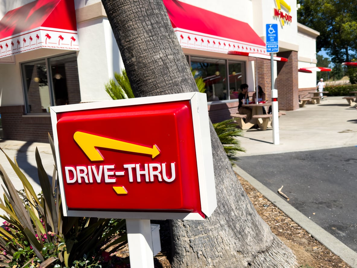 Red In-N-Out Burger drive-thru sign with a yellow arrow, located in front of the restaurant building.