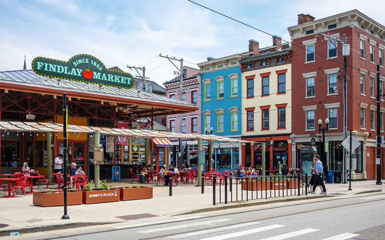 Findlay Market entrance with outdoor seating, flanked by colorful historic brick buildings along a city street.