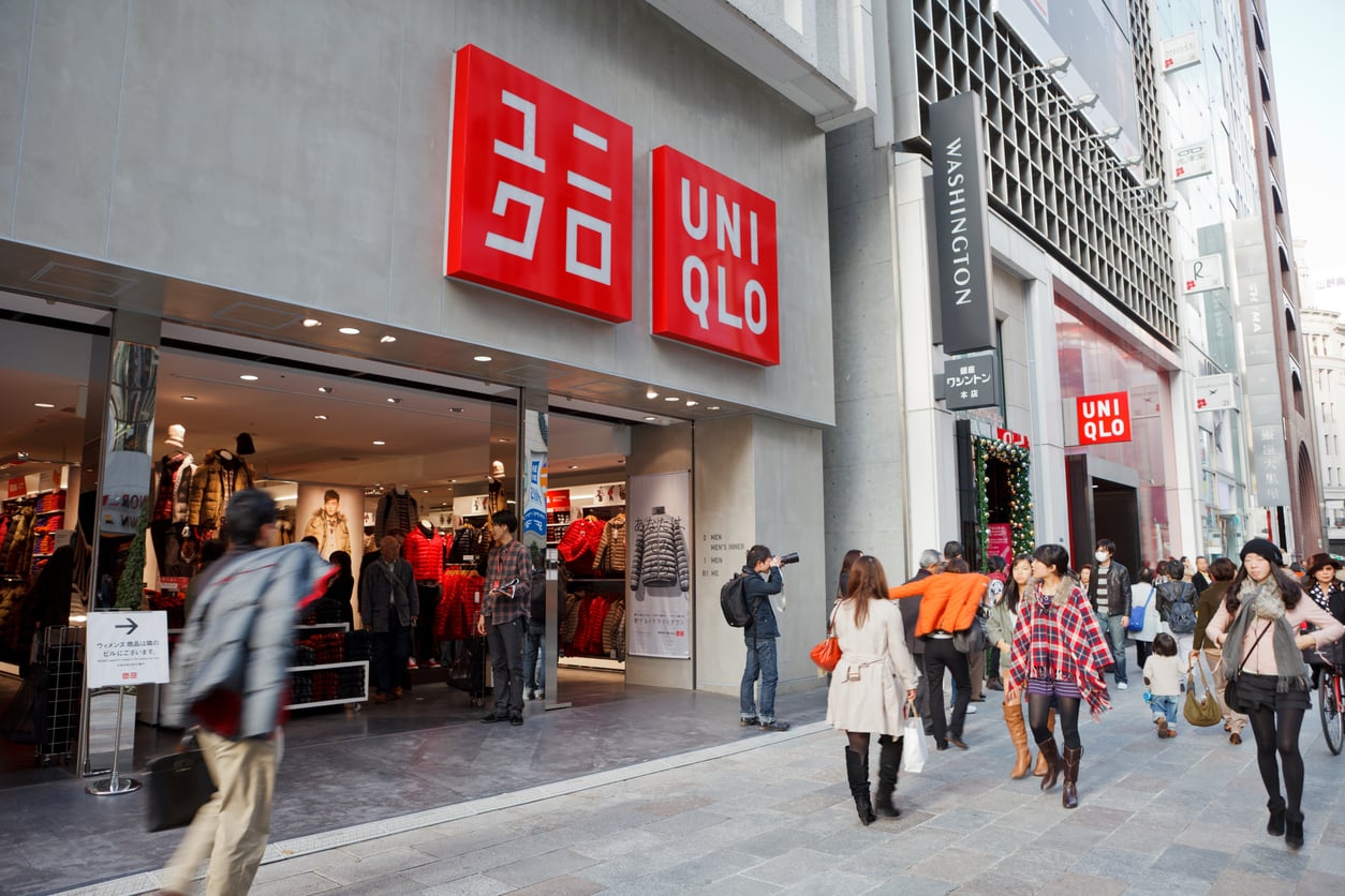 Pedestrians walking on a sidewalk in front of a Uniqlo store entrance with a large red logo.