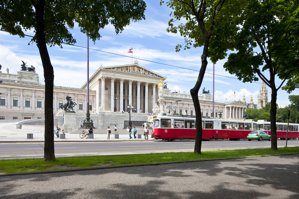 A red and white streetcar passes in front of the Austrian Parliament Building in Vienna, perfect for trips that feel luxurious.