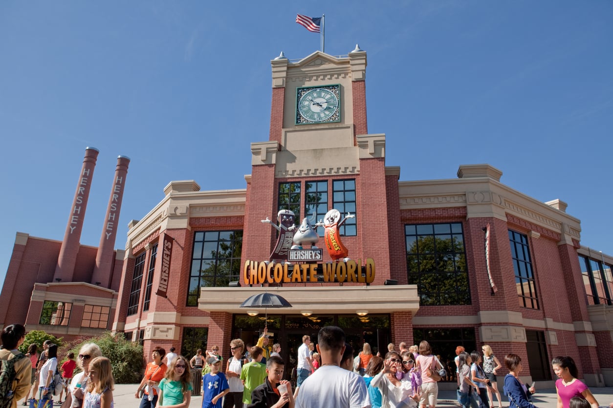 A crowd enters the Hershey’s Chocolate World building, a popular stop for food trips, beneath its iconic clock tower and giant candy mascots.