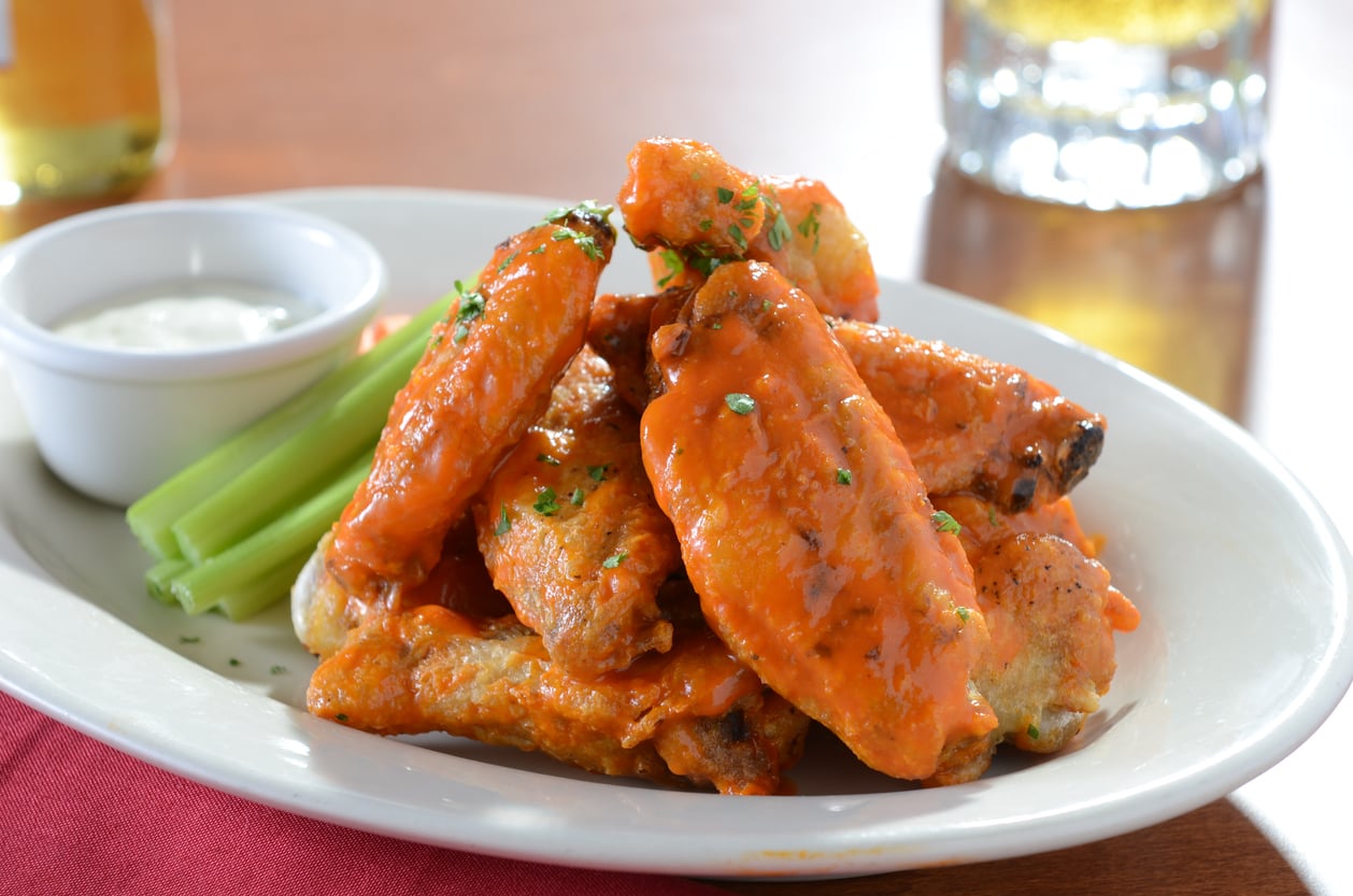 A plate of buffalo wings with a side of celery sticks and ranch dressing.