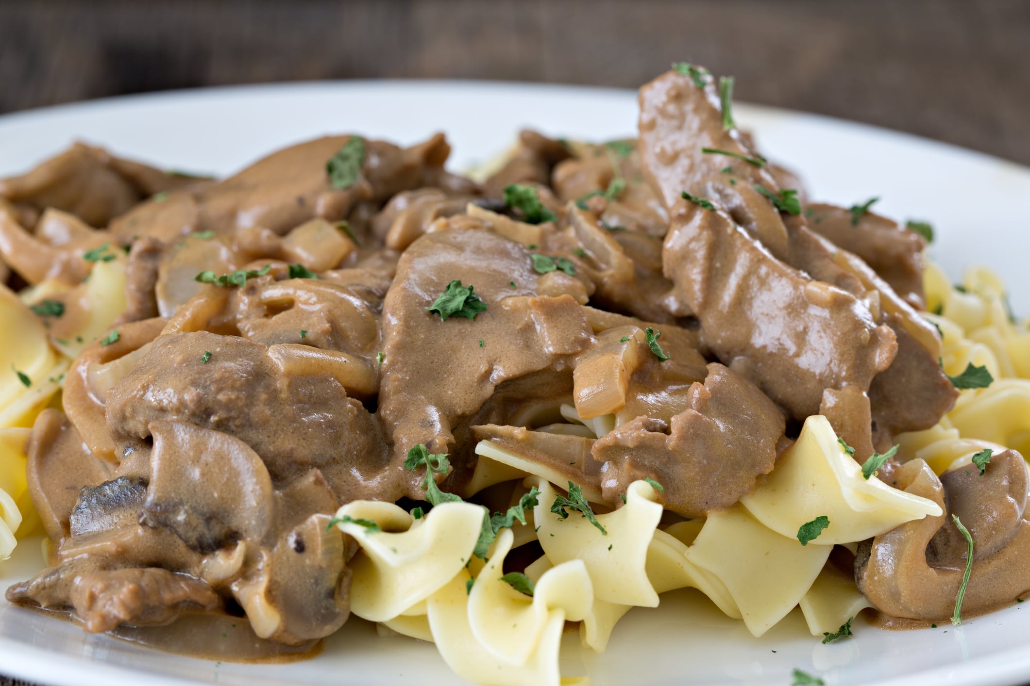 Beef stroganoff with mushrooms and sauce served over egg noodles, garnished with parsley.