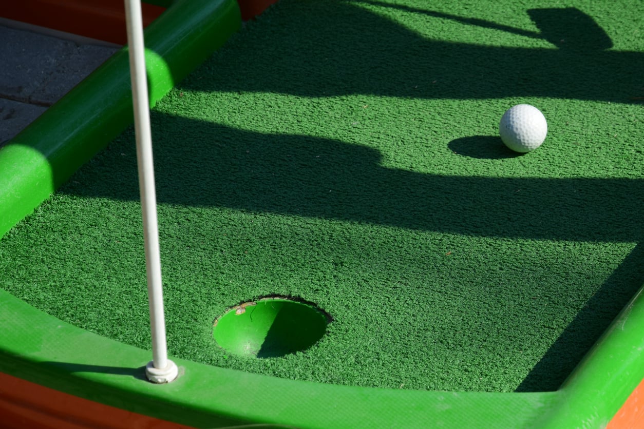 A white golf ball sits on a green putting mat near a hole and a flagstick, part of the cruise ship amenities.