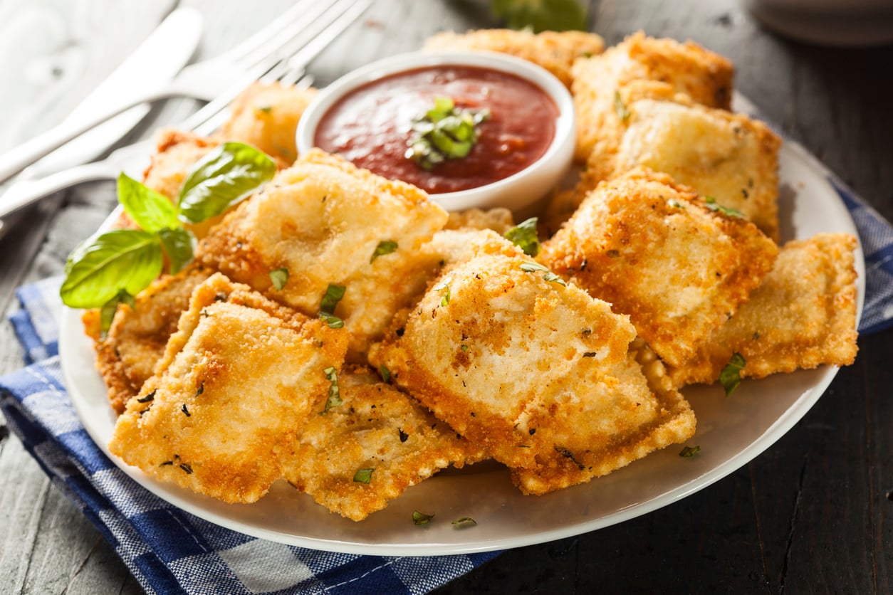 A plate of breaded, fried ravioli served with a small bowl of marinara sauce garnished with fresh basil.